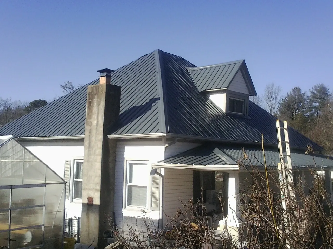 Dark blue standing seam metal roof on a white farmhouse with dormer — Slate & Tile Roof Repair by Roofing Brothers in Glenwood