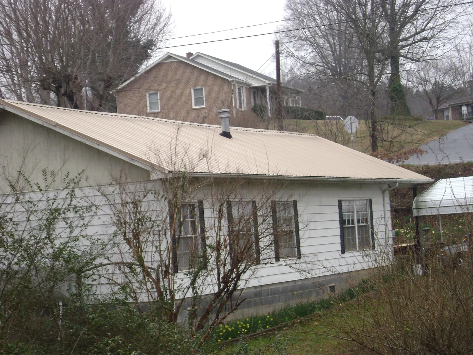 Tan metal roof on a white sided house set into a hillside — Commercial Roofing by Roofing Brothers in Glenwood